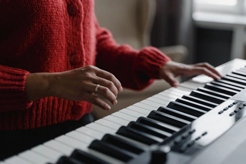 Mãos de uma mulher sobre o piano, com um blusão vermelho.