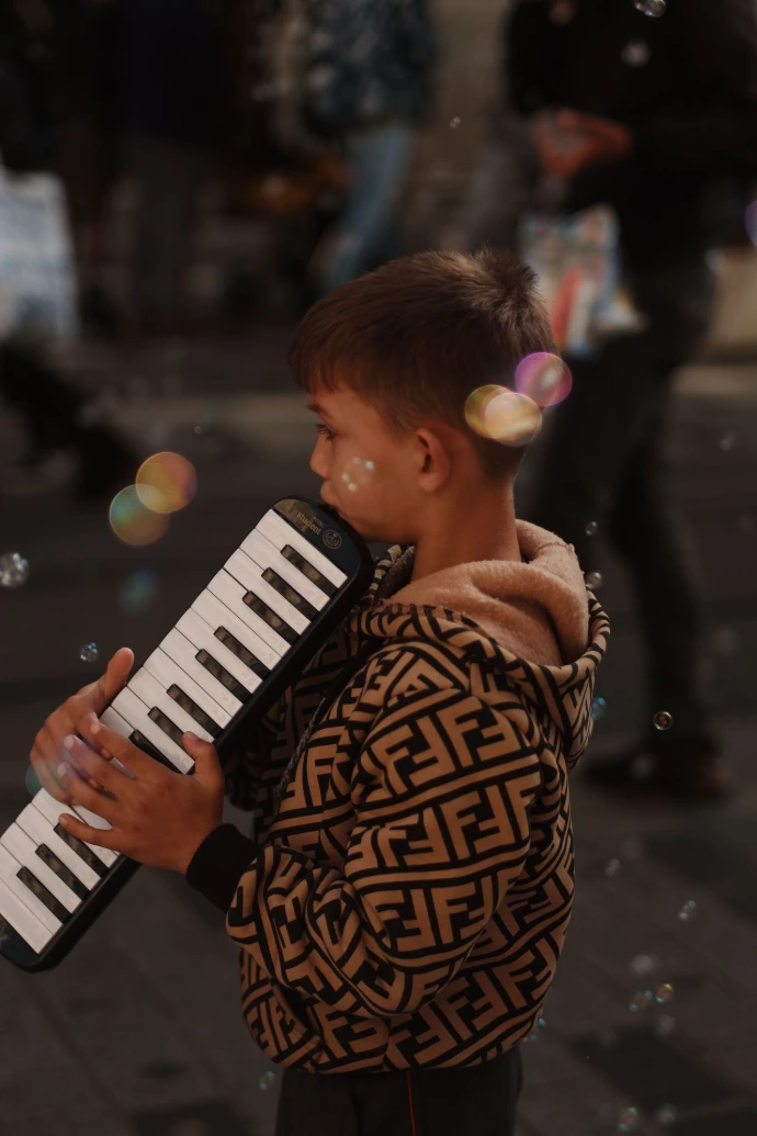 Menino tocando uma escaleta, ele está na rua.